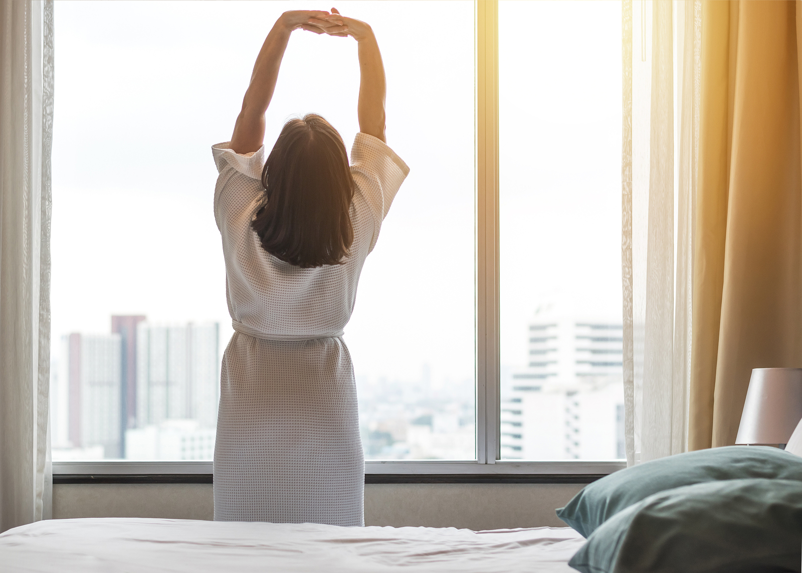 Easy weekend lifestyle woman waking up from sleep in the morning taking some rest relaxing in comfort bedroom at hotel window having a happy lazy day and enjoying work life quality balance concept