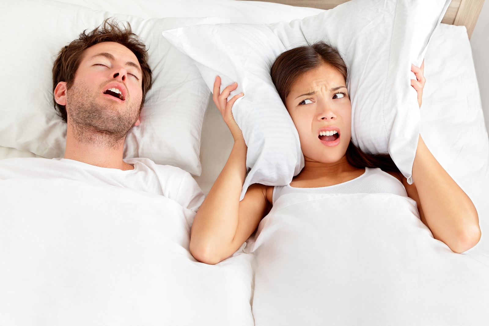 Snoring man Couple in bed man snoring and woman can not sleep covering ears with pillow for snore noise Young interracial couple Asian woman Caucasian man sleeping in bed at home